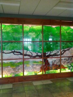 a large window with a tree painted on it's side in front of a tiled floor