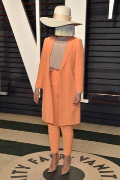 a woman in an orange suit and white hat standing on a black and white carpet