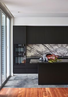 a kitchen with black cabinets and marble counter tops, along with wooden flooring that matches the walls