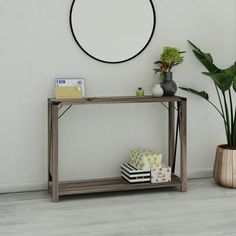 a table with a plant and some books on it next to a wall mounted round mirror