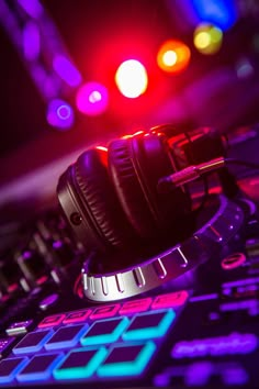 headphones resting on top of a dj's controller in front of colorful lights