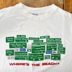 a white t - shirt with street signs on it that says where's the beach?