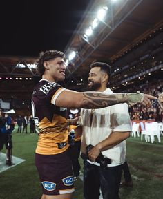 two men are shaking hands on the field at a football game with fans in the stands