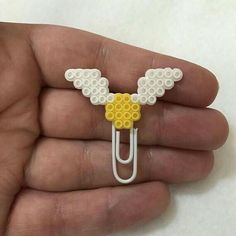 a hand holding a white and yellow lego style paper clip with an angel design on it