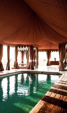 an outdoor swimming pool in the middle of a large open area with curtains over it