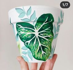 a hand holding up a cup with green leaves painted on the outside and inside it