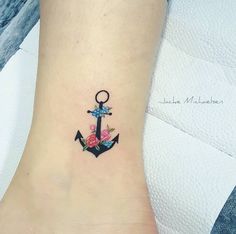 an anchor tattoo with flowers on the side of the ankle, and a ring in the middle