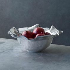 a metal bowl filled with red apples on top of a marble countertop next to a gray wall