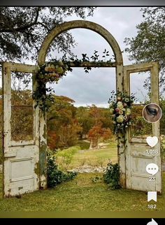 an open door with flowers on it in the middle of a grassy field and trees