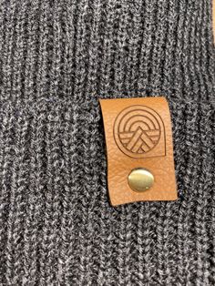 Give the gift of warmth and style! This knit beanie is perfect for hiking, camping, and perfect for keeping warm! Beanie is a dark charcoal gray color, and is made of a soft wool/acrylic blend. Attached is an engraved leather label tag with a brass rivet. The leather label is engraved on both sides, so whether you wear the hat with the brim up or down, the label will still show the design in the correct orientation. Choice of circle logo or trees available at checkout. Care - Hand wash, dry flat Gray Winter Hats For Outdoor, Gray Winter Outdoor Hats, Outdoor Beanie Cap, One Size Fits Most, Windproof Beanie For Fall, Windproof Beanie For Outdoor, Warm Gray Hats For Outdoor, Warm Gray Hat For Outdoor, Outdoor Windproof Beanie, Knitted Beanie For Outdoor