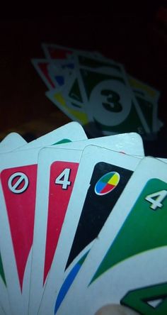 a hand holding four playing cards with numbers and symbols on them, all in different colors