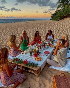 a group of women sitting around a table on the beach