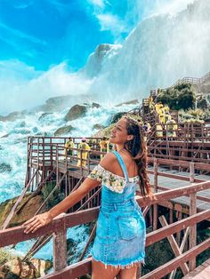 a woman standing on top of a bridge next to the ocean in front of a waterfall