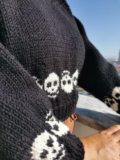 a person wearing a black and white sweater with skulls on it's sleeves, holding a cell phone in their hand