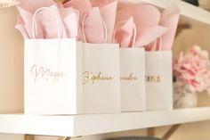 pink roses are in white paper bags with gold lettering on the top and bottom, along with other small gift bags