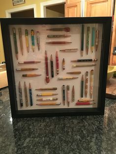 a framed display with pens and pencils in it's shadow box on a marble countertop