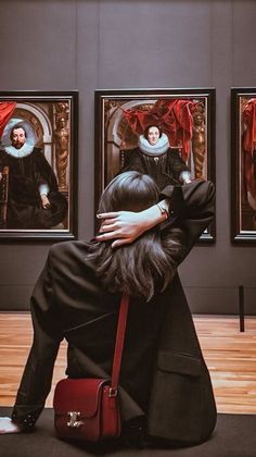 a woman sitting on the ground in front of paintings with her back to the camera