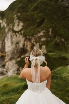 the back of a bride's dress as she stands in front of a cliff