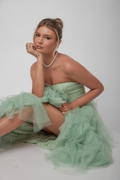 a woman in a green dress sitting on the floor with her hand under her chin