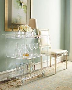 a bar cart with wine glasses and bottles on it in front of a wall painting