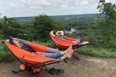 two people laying in orange hammocks on top of a hill