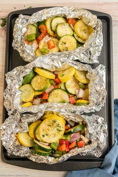 three foil packets filled with vegetables on top of a pan covered in aluminum foil next to a wooden table