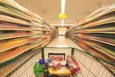 an empty shopping cart in a grocery store filled with food and drinks as motion blurs behind it