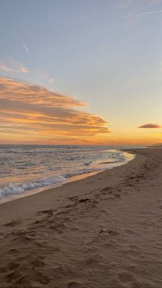 the sun is setting at the beach with footprints in the sand