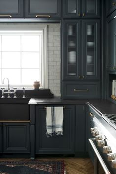 a kitchen with black cabinets and white brick backsplash, an area rug on the floor