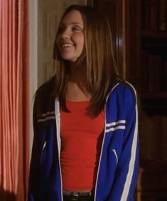 a young woman standing in front of a door wearing a red shirt and blue jacket