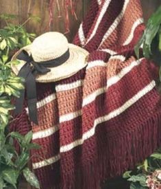 a red and white blanket sitting on top of a wooden bench next to green plants