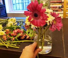 a person is arranging flowers in a vase on a table with other flowers and books