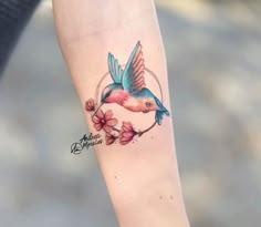 a small bird tattoo on the left forearm and right arm, with pink flowers around it