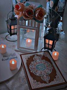 a table topped with lots of lit candles next to a box filled with paper flowers