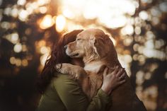 a woman holding a dog in her arms with the sun shining through the trees behind her