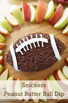 a football shaped cake with chocolate sprinkles and apples around it on a cutting board