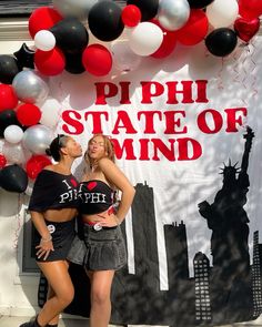 two women standing in front of a sign with balloons