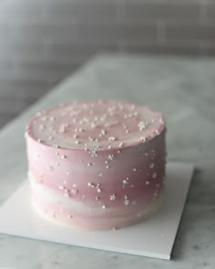 a pink cake with white sprinkles on it sitting on top of a table