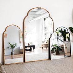 three mirrors sitting on top of a wooden floor next to a plant in a vase