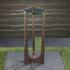 a glass and metal table with grass on the ground in front of a body of water