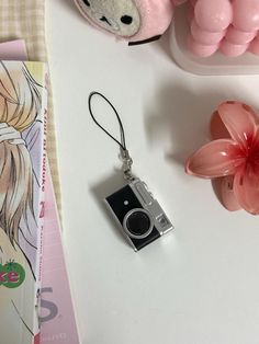 a camera keychain sitting on top of a table next to a pink flower