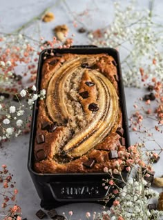 a loaf of chocolate chip banana bread on a baking pan with flowers in the background