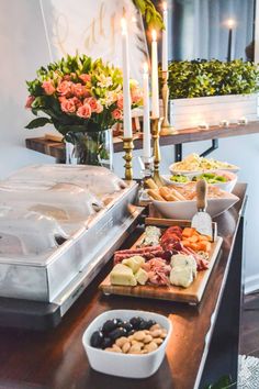 an assortment of food is displayed on a buffet table with candles and flowers in the background