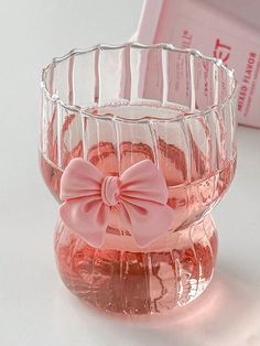 a glass vase with a pink bow on the front and bottom, sitting next to a book