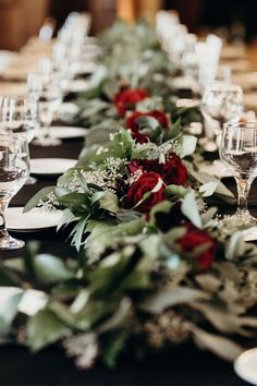 a long table is set with white and red flowers, greenery and wine glasses