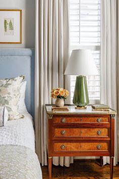 a bedroom with a bed, nightstand and lamp on it's side table in front of the window