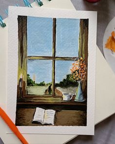 an open book sitting on top of a table next to a window with flowers in it