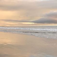 a person walking on the beach with a surfboard in their hand and clouds in the background