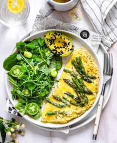 a white plate topped with an omelet and asparagus next to a cup of tea