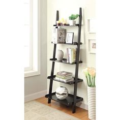 a black leaning shelf with books and vases on it in front of a white wall